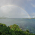 Semi-circle rainbow over blue water against a blue sky