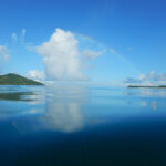 White cloud and a rainbow with a reflection in the blue sea