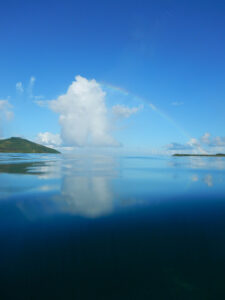 White cloud and a rainbow with a reflection in the blue sea