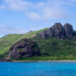 Island hill studded with volcanic rocks and blue water in the foreground