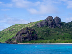 Island hill studded with volcanic rocks and blue water in the foreground