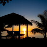 Cabana containing 2 lounge chairs by the water at sunset