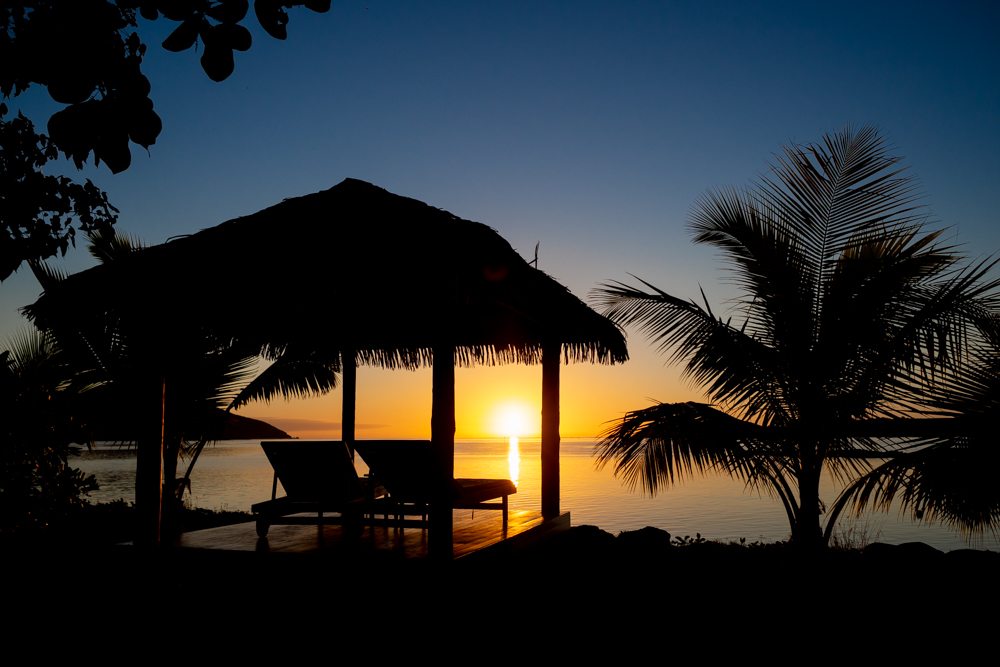 Cabana containing 2 lounge chairs by the water at sunset