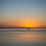 Single distant small motor boat crosses the horizon against the setting sun