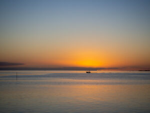 Single distant small motor boat crosses the horizon against the setting sun