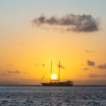 Setting sun between two masts of a double-masted yacht