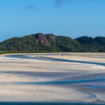 White sand swirled with blue ocean water against a blue sky backdrop