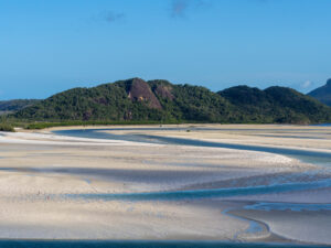 White sand swirled with blue ocean water against a blue sky backdrop