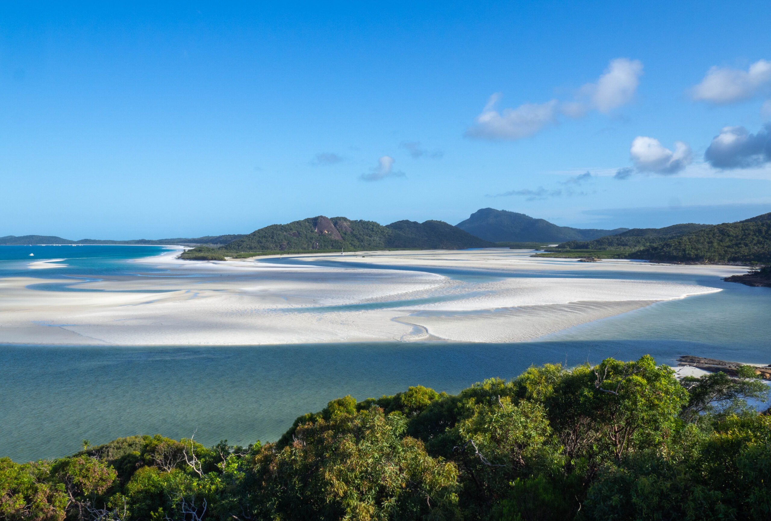 White sand swirled with blue ocean water against a blue sky backdrop