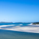 White sand swirled with blue ocean water against a blue sky backdrop