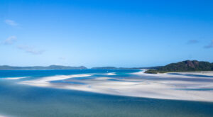 White sand swirled with blue ocean water against a blue sky backdrop