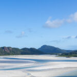 White sand swirled with blue ocean water against a blue sky backdrop