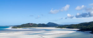 White sand swirled with blue ocean water against a blue sky backdrop